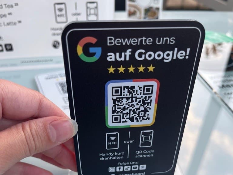 Ein Aufsteller in der Hand: „Bewerte uns auf Google!“ mit QR-Code in den Google-Farben, ein Beispiel-Design