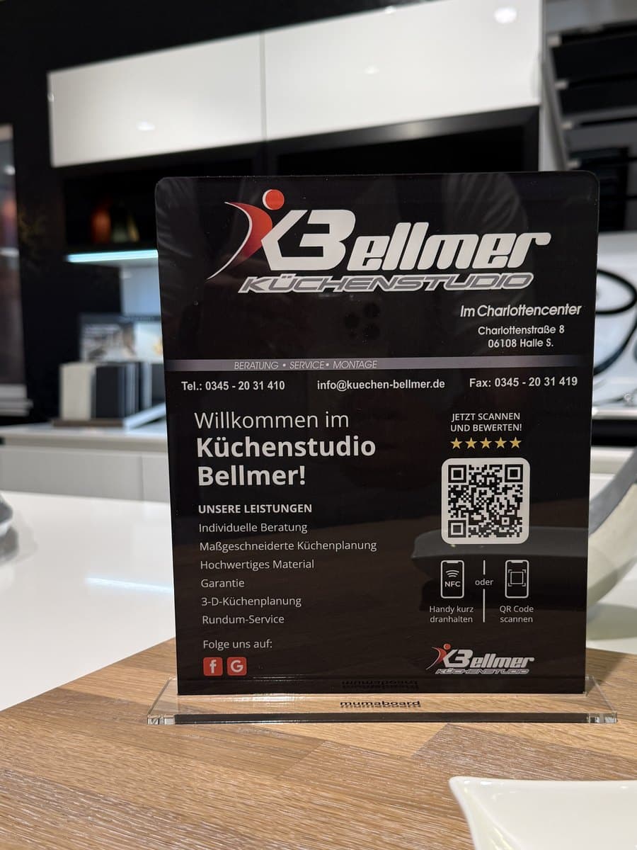 Der große Aufsteller des Küchenstudios Bellmer auf dem Standfuß auf dem Tresen: „Willkommen im Küchenstudio Bellmer!“ mit Leistungen, QR-Code und NFC