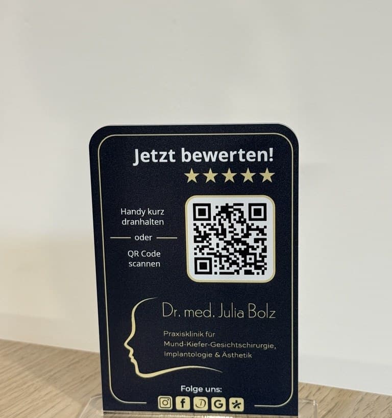 Ein Aufsteller auf dem Standfuß auf einem Holztisch: Jetzt bewerten!, in Schwarz und Gold, der Praxisklinik Dr. Julia Bolz