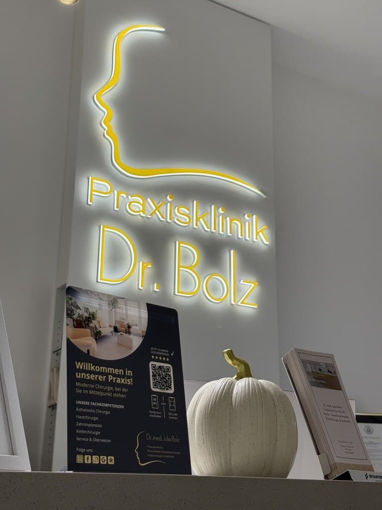 Der große Aufsteller der Praxisklinik Dr. Julia Bolz am Empfang unter dem leuchtenden Logo: „Willkommen in unserer Praxis!“ mit QR-Code und NFC