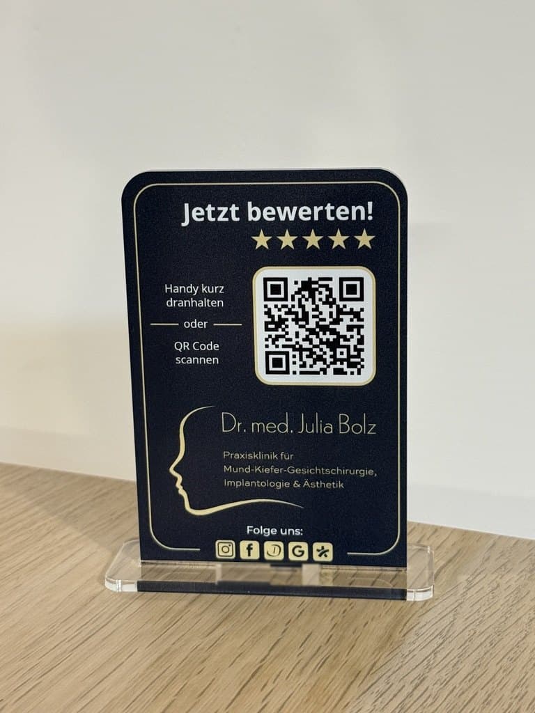 Der Mini-Aufsteller der Praxisklinik Dr. Julia Bolz auf dem Standfuß: „Jetzt bewerten!“ in Schwarz und Gold mit QR-Code